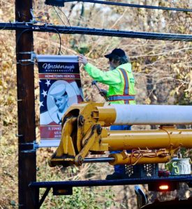 A Northborough DPW worker hangs a veterans banner produced by Boros Cares 4 Troops, last year