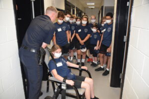 Cadet Arianna Anderson volunteers to demonstrate the restraint chair as Lt. Dan Campbell adjusts the straps.