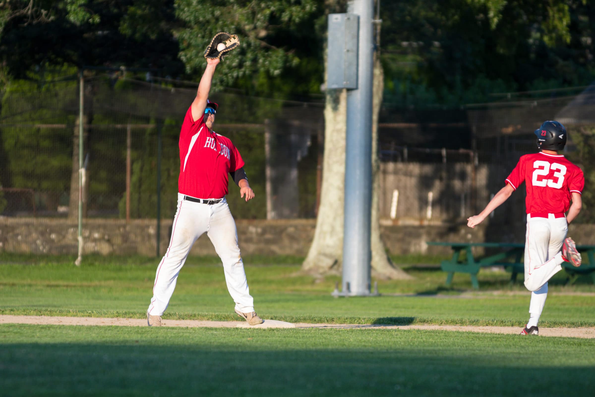 Hudson’s first basemen stretches to catch a throw from a teammate as their Natick opponent runs to beat the play.