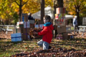 Child plays in leaf pile with leaves. Boxes in the background. Autumn.