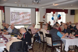 Group luncheon with "thank you" on screen with American Flag in background