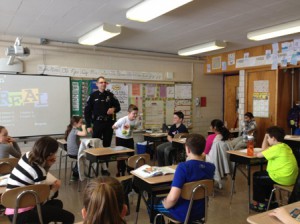 During a Peaslee 5th grade D.A.R.E. lesson, Officer Martin performs a handcuff demonstration on volunteer student, Ryan Bourcher.  Julia Howe (left) and Joe Scangas (right) watch eagerly along with the rest of their classmates. 