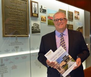 Craig DeWallace displays the commemorative book, “Shrewsbury Public Library; Building the Next Chapter,” as he stands in front of the “Honoring the Past” display in a main floor hallway.