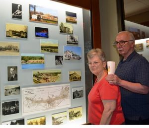 The history and donor wall are visible through a large window to the right of the library entrance. Sue and Tom Falzoi admire the section called “Building the Next Chapter.”