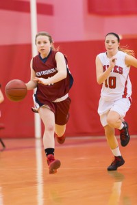 Westborough’s Jenna Lewis-Keddy (red #11) races down the court with the ball while being pursued by Hudson’s Maclaine Campbell (white #10).