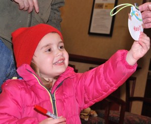Abigail Hurtley, 4, is pleased with the snowman ornament she created with help from Hudson Garden Club members at Avidia Bank.