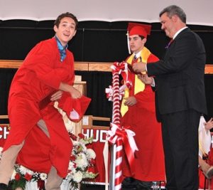 Justin Melo (left) aims to toss his cap after receiving his diploma from Principal Brian Reagan (right) assisted by Class President Dennis Panneton (center). 