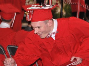 Tom O’Loughlin holds his diploma with one hand and fist bumps with the other.