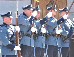 A state trooper color guard unit stands at attention as the casket passes.