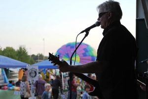 Bruce Marshall sings early in his concert at the Balloons and Blues Festival while a balloon rises in the background. After gusty winds had prompted the cancellation of an early evening flight, many of the balloons were able to inflate while Marshall performed. 