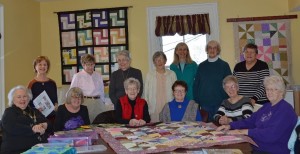 Members of the Hudson Silver Threads Quilters ready themselves for their weekly Thursday meeting. Behind them on the left wall is their first group project, a rail fence quilt. On the right, the display changes monthly. January’s wall hanging was designed and made by founding member Sally Mau. (Photo/Joyce DeWallace)