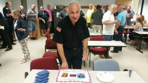Larry Bastien, retiring from his position as the city’s dispatcher, prepares to cut the cake at a farewell gathering in his honor.