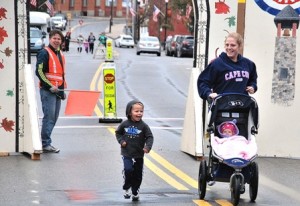 (l to r) Highland City Strider member Dan Milton encourages A.J. May, 3, and his mother Laura with Rebecca, eight months, in the stroller as they near the finish line of the Main Street Mile.