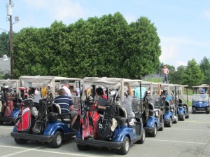 Photo 1: Golfers lined up in carts, waiting to tee off.