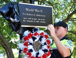 At the World War II – Korean War – Vietnam War Memorial, Officer Nathan Fiske unveils a plaque honoring Private Robert E. Robertson, who was killed in action at age 18 in World War II.