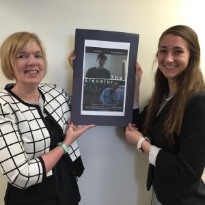 Nancy Swanberg (left), executive director of the Northborough-based nonprofit agency, Friendship Network for Children, joins Tiffany Kline, the agency’s service coordinator, to hold the movie poster for the Friendship Network’s film, “The Elevator.” (Photo/Lori Berkey)
