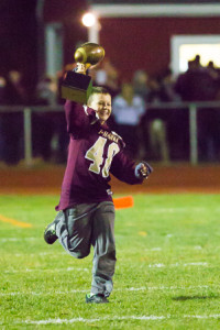 John Valentine runs onto the field showing off the team’s championship trophy during halftime of the Algonquin Regional football game against Fitchburg Nov. 13. Photo/Jeff Slovin