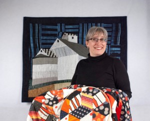 Mary Walter, holding a work in progress, stands in front of one of her finished quilts. (Photo/submitted)