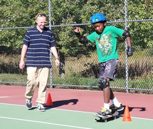 Paul Ferguson coaches fifth-grader Logan Matthews as he skateboards around an obstacle course of cones.