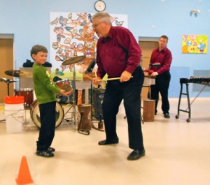 First-grader Christian Campero holds a resonating chamber while Bob Otto uses sticks to play it.