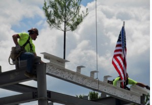 The final beam, complete with pine tree, flag and signatures, is carefully set in place by two workmen at the recent topping off ceremony.
