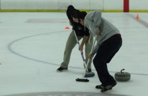 Two curlers at the Aug. 7 open house sweep ahead of a stone. The first half of the open house was devoted to throwing stones. The second half taught attendees how to sweep to make stones go farther. (Photo/Dakota Antelman)