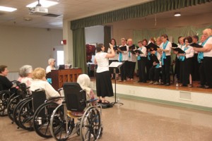 Wendy Damoulakis, center, and the women of the Hundredth Town Chorus perform for an audience at St. Patrick’s Manor in Framingham. (Photo/Alex Cornacchia)