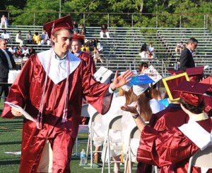 Zach Tretter carries his diploma with one hand and high fives another graduate with the other.