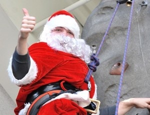 Santa Claus reaches the top of the rock wall.